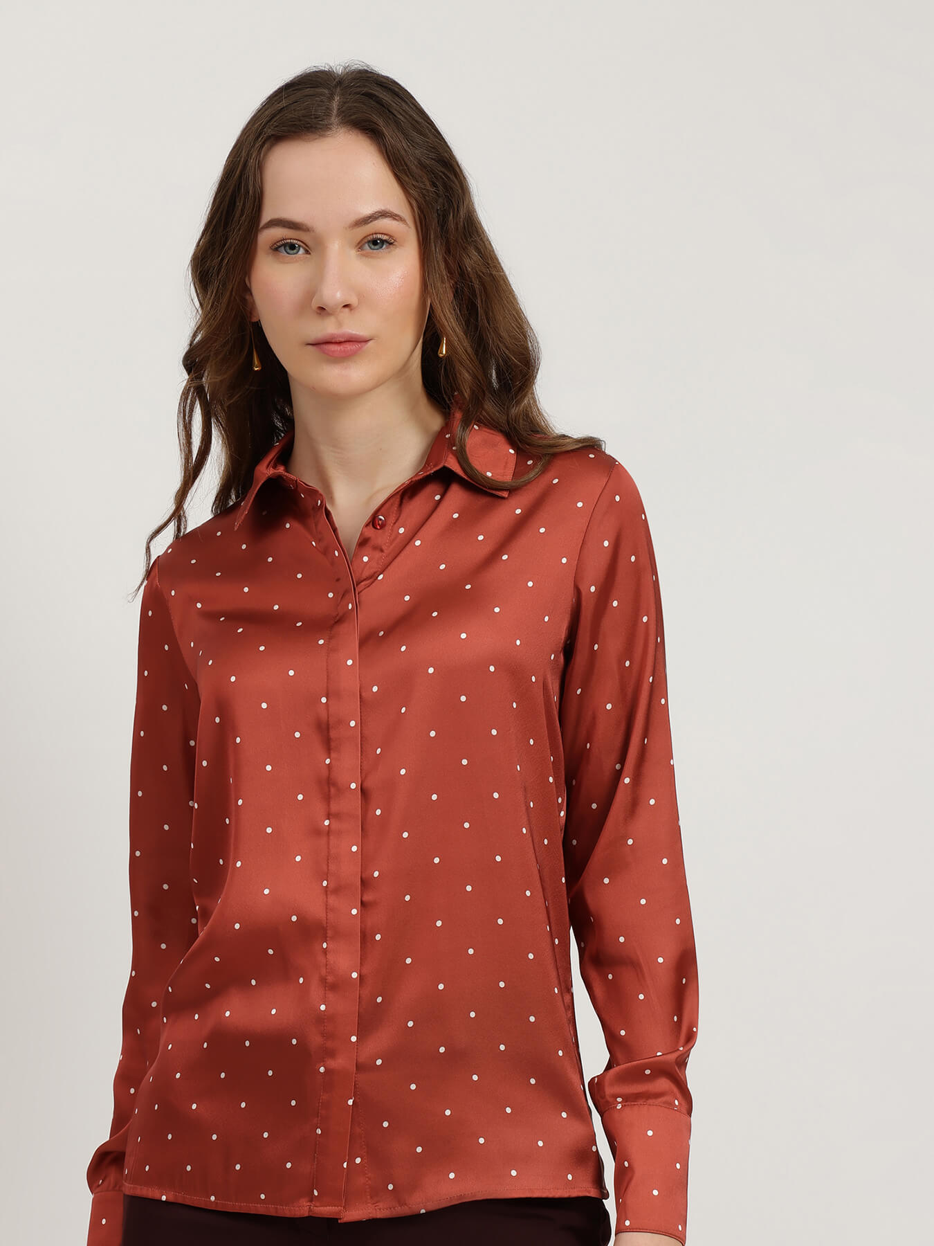 Woman wearing a rust-colored shirt with white polka dots on a plain background