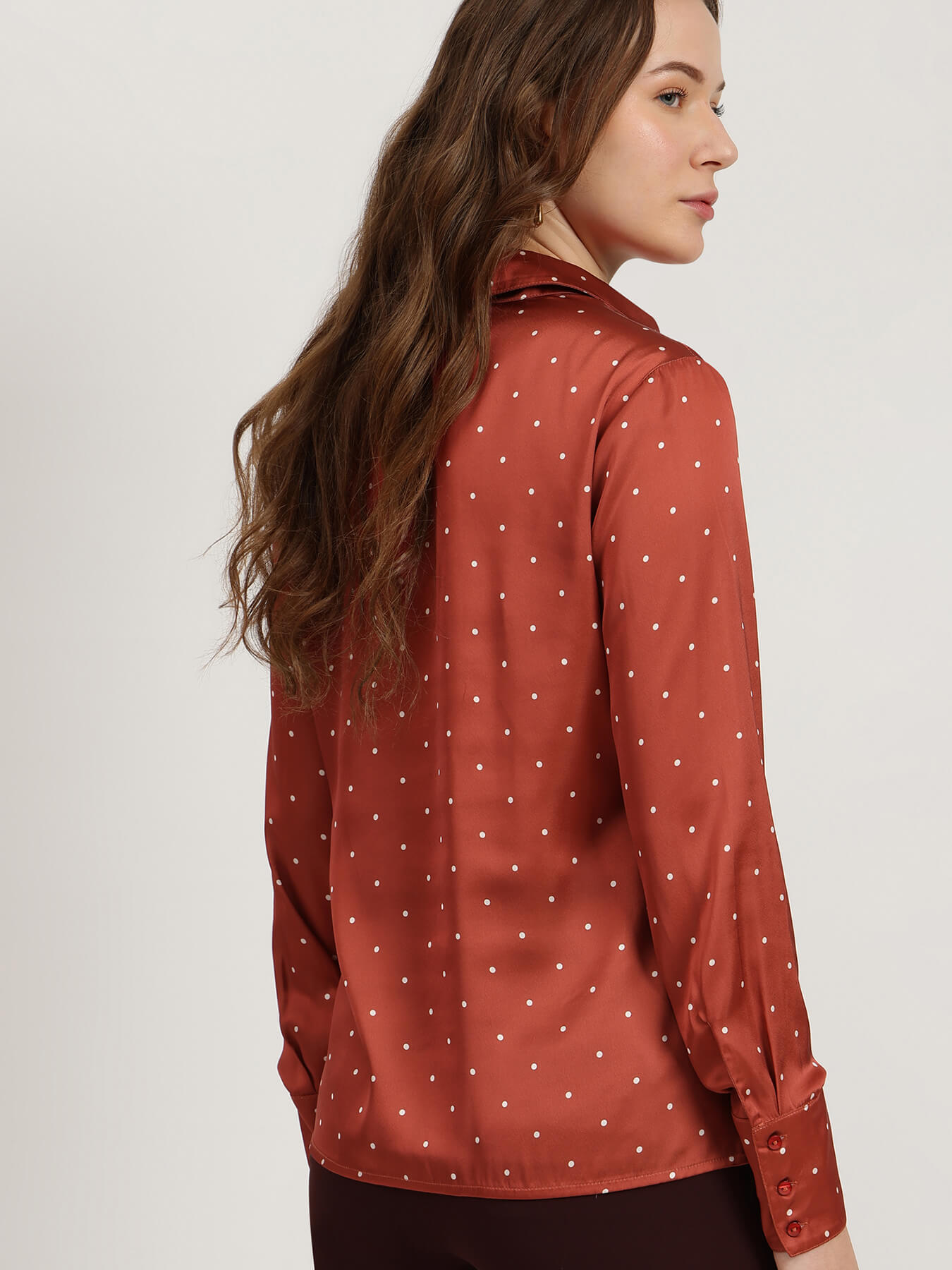 Woman wearing a rust-colored blouse with white polka dots on a plain background