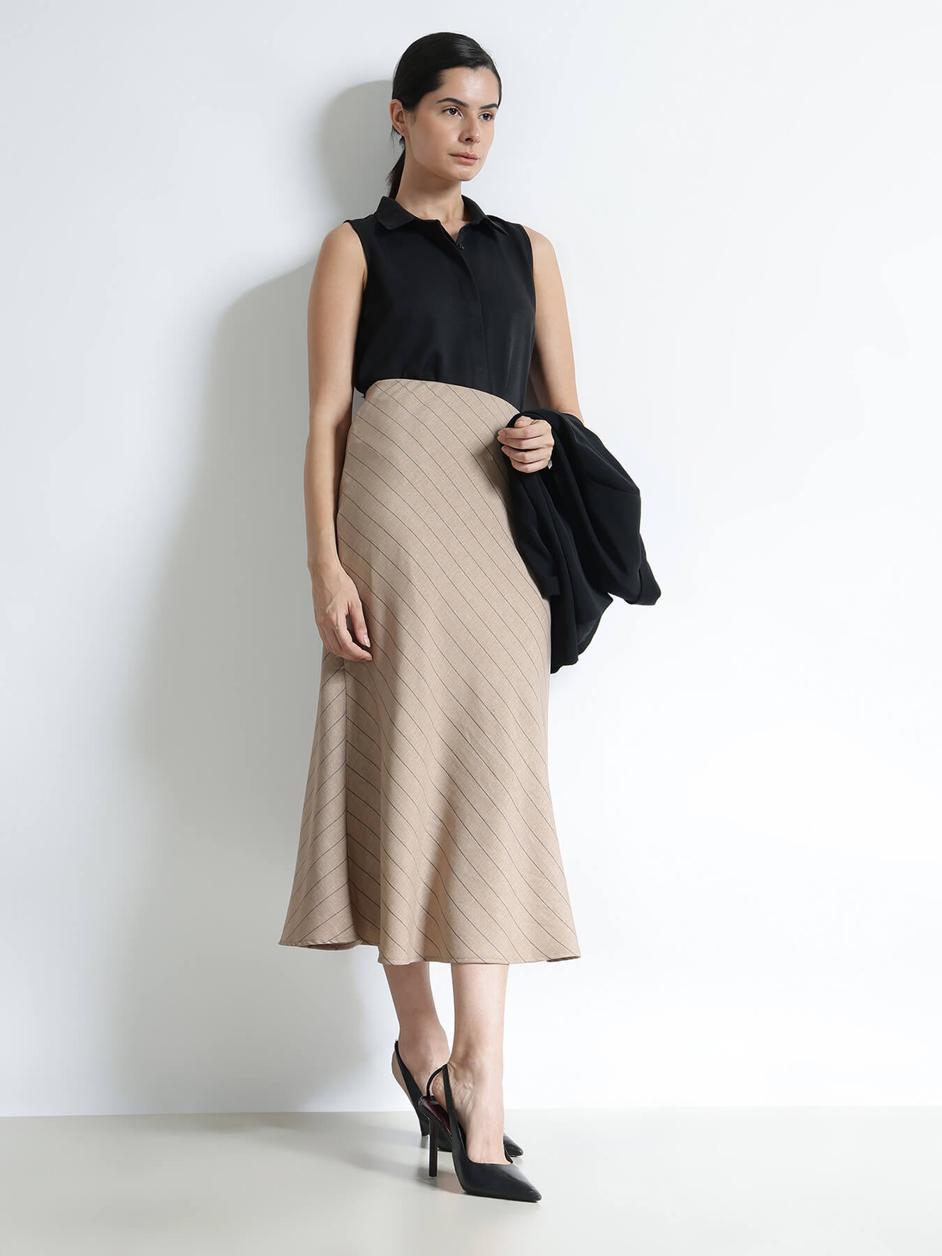 Woman wearing a black sleeveless top and beige skirt against a white background