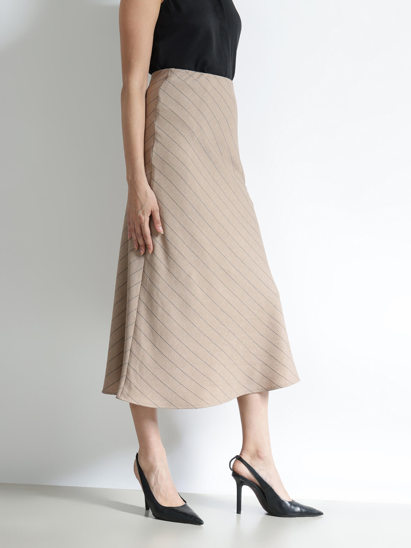Woman wearing a beige pleated skirt and black high-heeled shoes on a white background