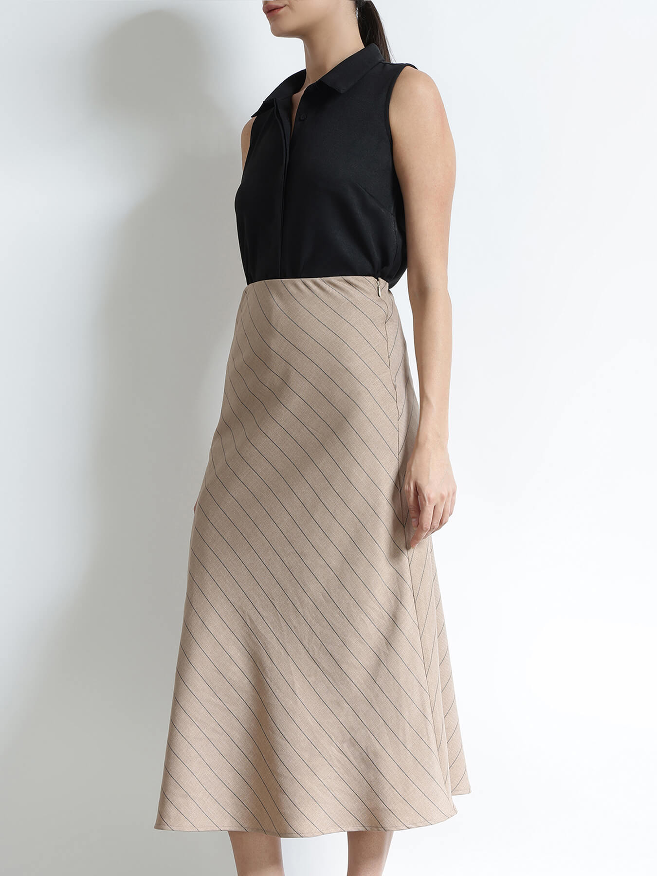 Woman wearing a black sleeveless top and beige pleated skirt against a white background