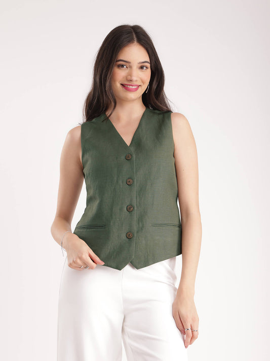 A woman wearing a green linen waistcoat with V-neck and 2 front pockets, paired with white trousers.
