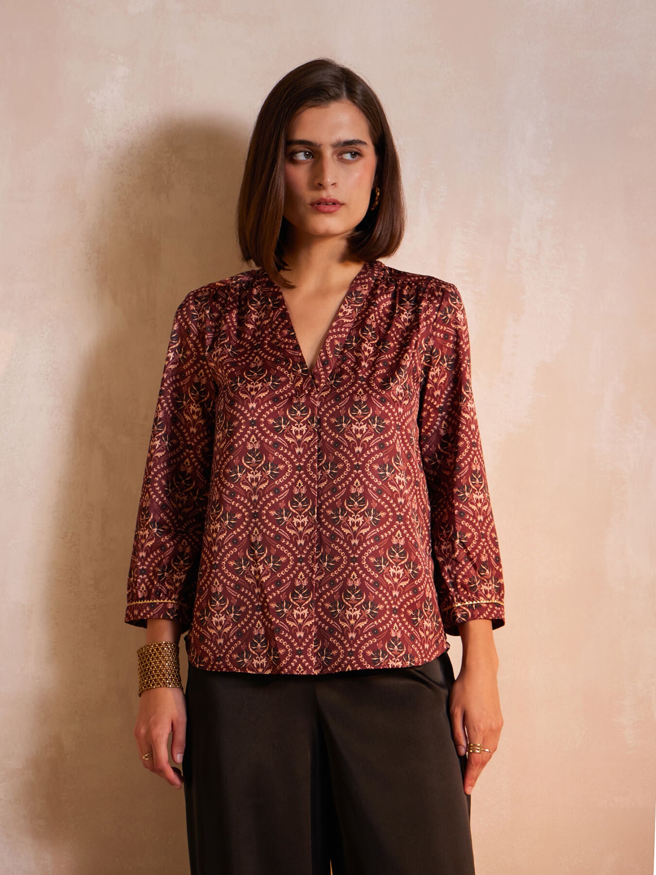 A woman wearing a maroon satin top with festive motif print, featuring a v-neck and three-quarter sleeves.