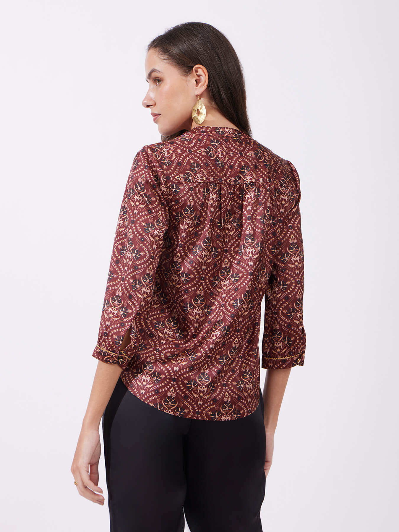 A woman wearing a maroon satin top with festive motif print, featuring a v-neck and three-quarter sleeves.