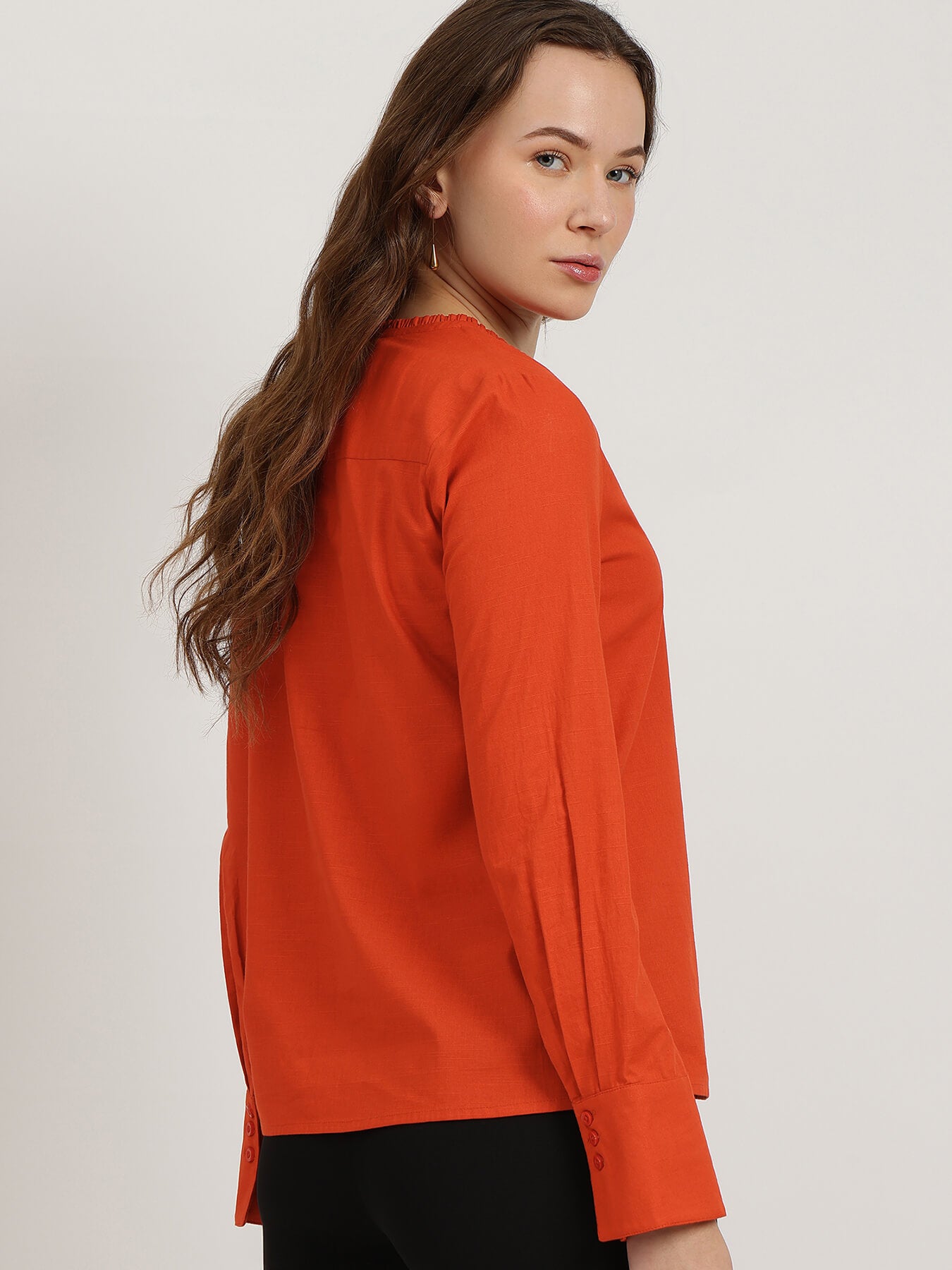 Woman wearing an orange long-sleeve top against a plain background