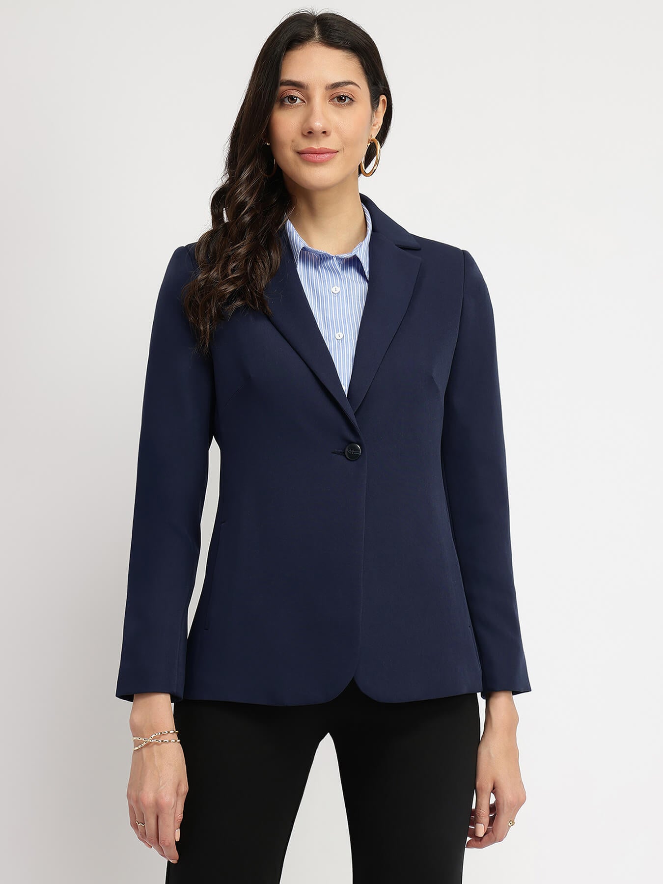 Woman wearing a navy single breasted blazer with a notch collar, fully lined, with two pockets, long sleeves, and a non-transparent fabric.