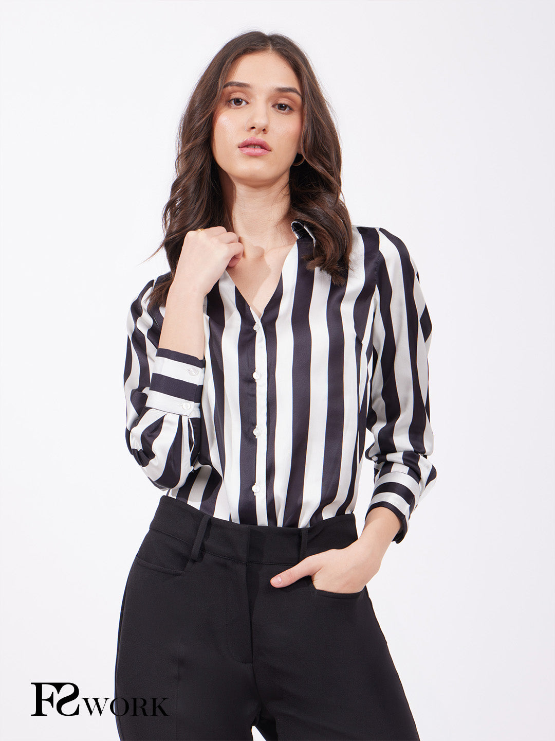 A woman wearing a black and off white striped satin shirt with a collared V-neck and long sleeves, paired with black pants.