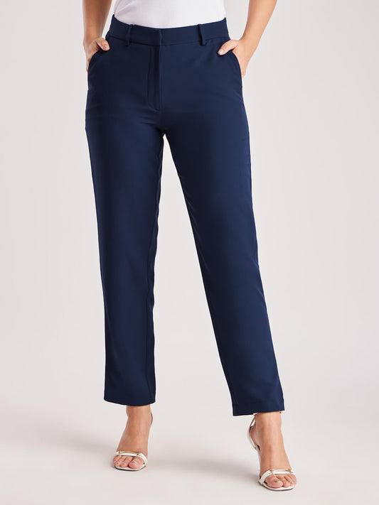 A person standing wearing navy blue straight fit trousers with pockets, paired with a white top and light-colored shoes.