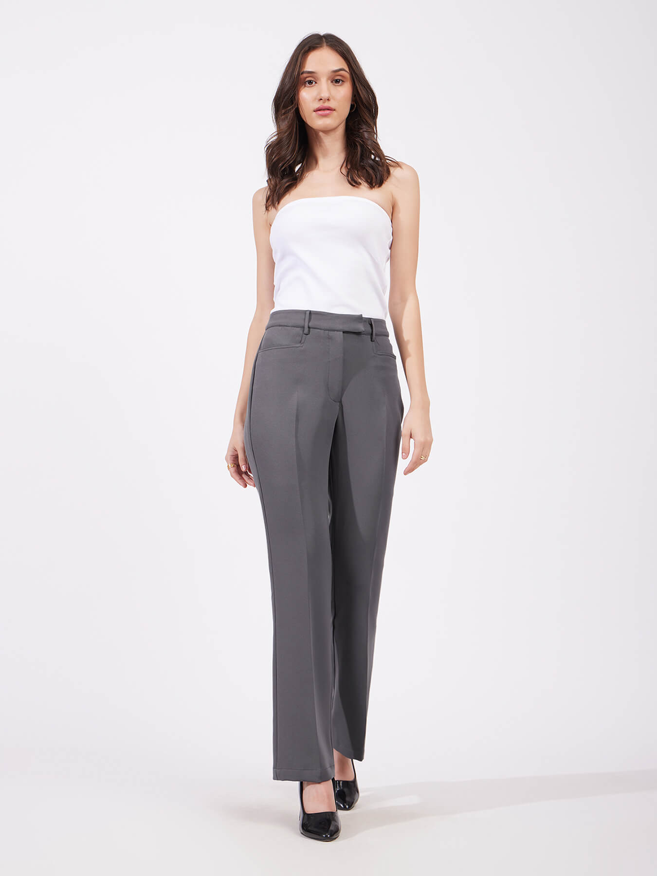 A person standing wearing grey bootcut trousers with a high rise waist and side pockets, paired with a white top.