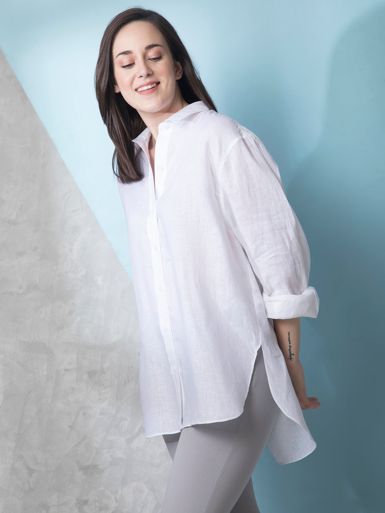 A woman smiling, wearing a white oversized collared shirt with long sleeves and a button placket.